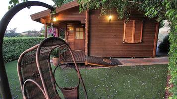 A wooden cabin with a porch, a swing chair, and a well-maintained lawn.