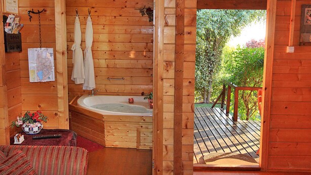 A wooden cabin with a bathroom featuring a bathtub, towels, and a map on the wall. - Eden Ramot Chalets (Ramot)
