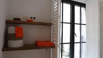 Quarto com piso branco, tapete vermelho, estantes de madeira com cestos organizadores e uma porta de vidro deslizante que dá para o exterior.