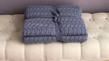 A folded blanket with a textured pattern, tied with a ribbon, placed on a tufted sofa.