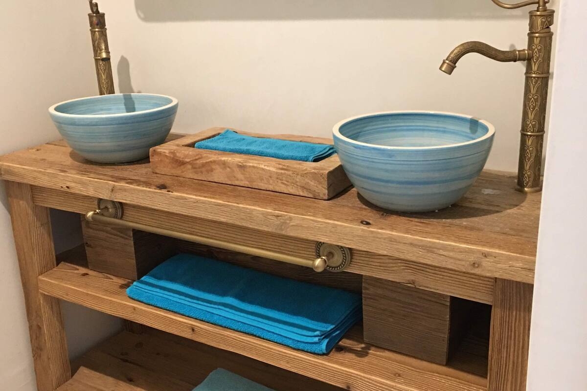 A wooden vanity with two blue ceramic bowls, a towel, and a brass faucet.