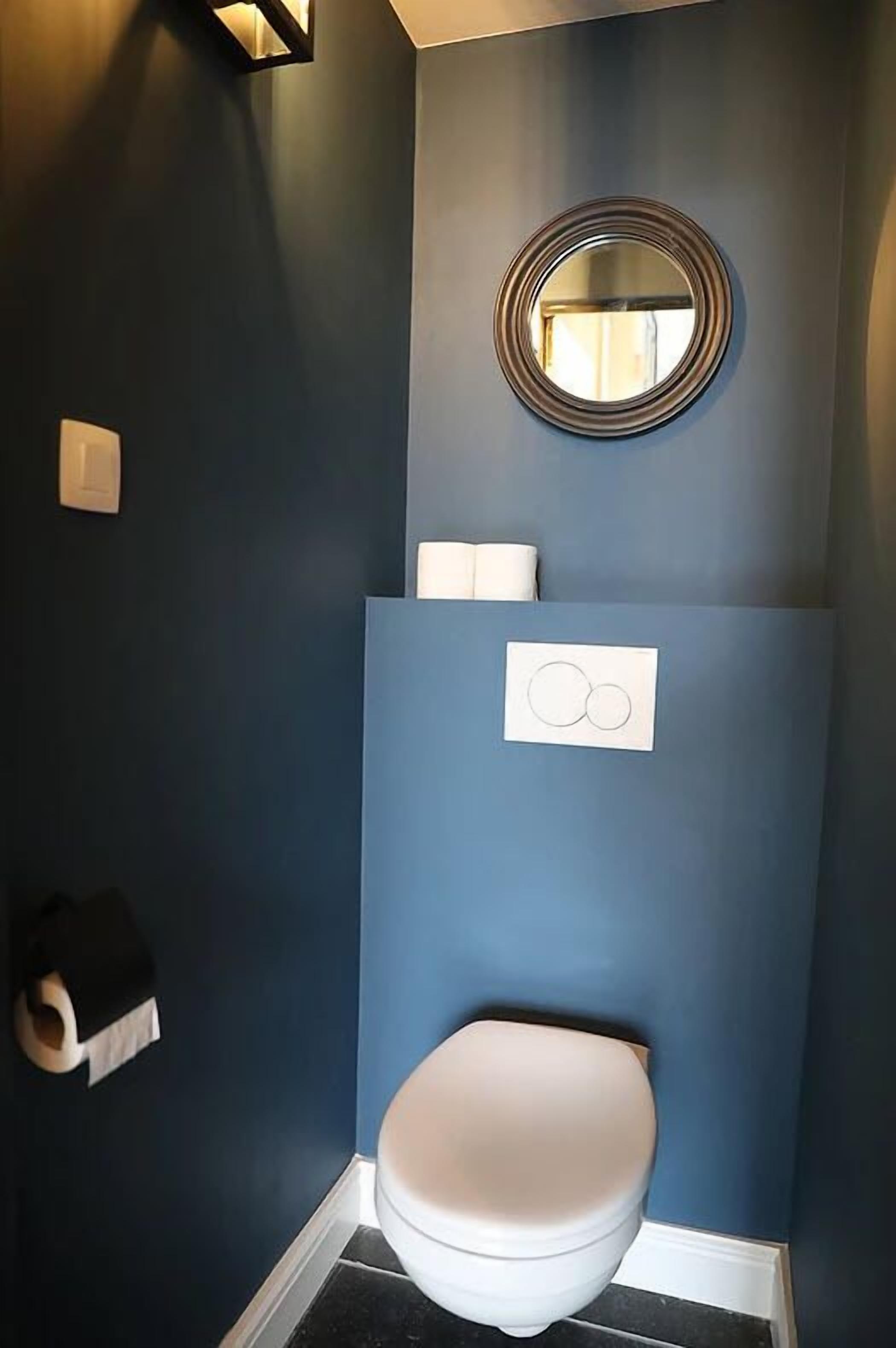 Un baño con inodoro, espejo y dispensador de toallas.