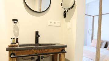 Un baño con tocador de madera, un espejo redondo, un espejo de mano y un farol.