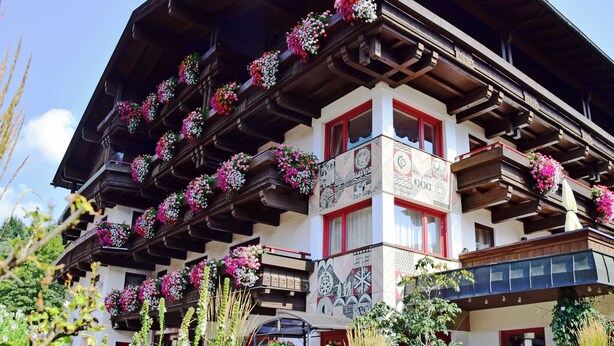 A traditional chalet with multiple balconies adorned with colorful flowers, a distinct architectural style, and a sign indicating a restaurant. - Hotel & Art Kristiana (Saalbach-Hinterglemm)