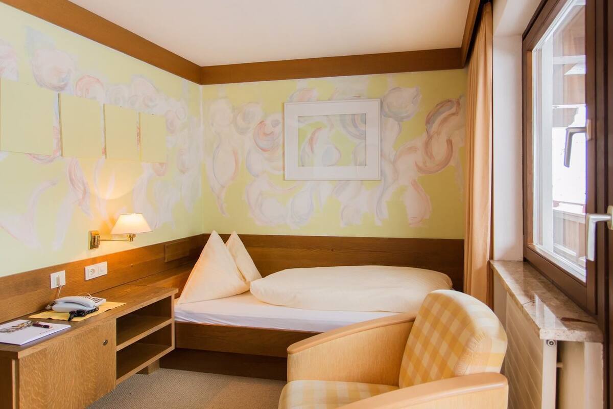 A hotel room with a bed, a desk with a lamp, a chair, and a window.