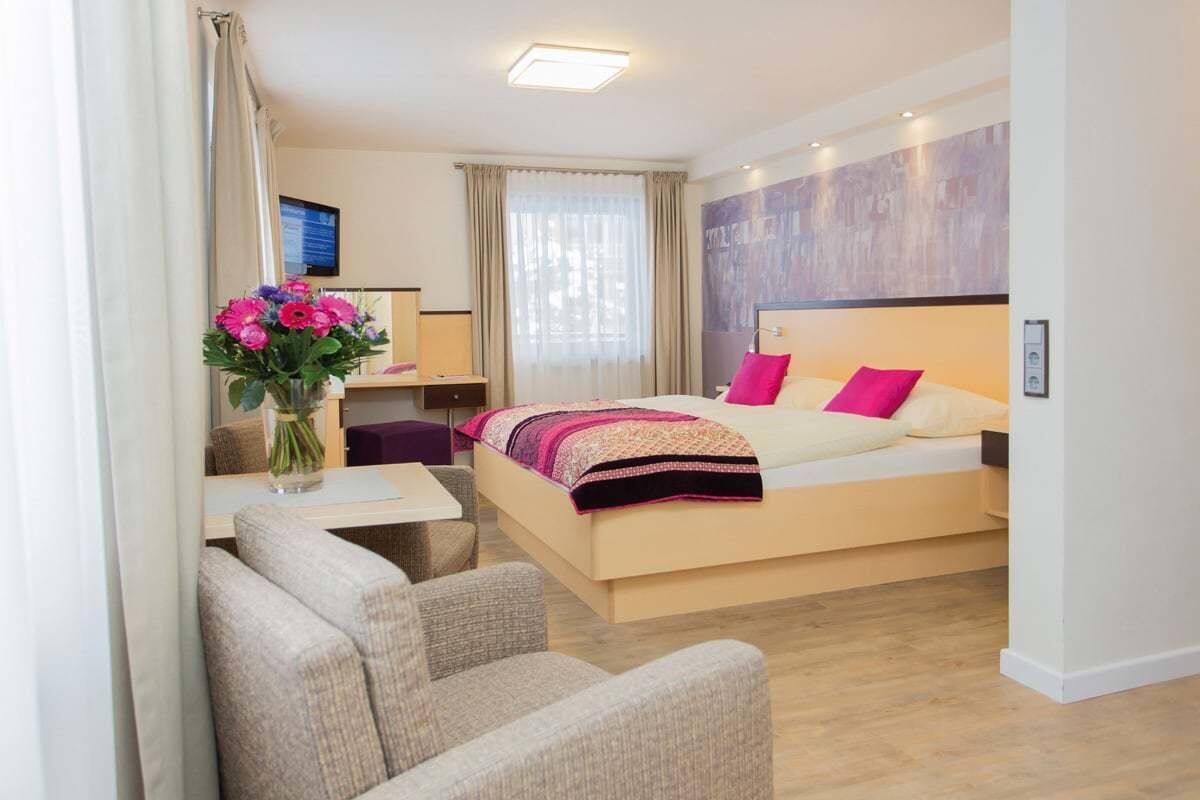 A modern hotel room with a bed, a desk, a chair, and a vase of flowers.