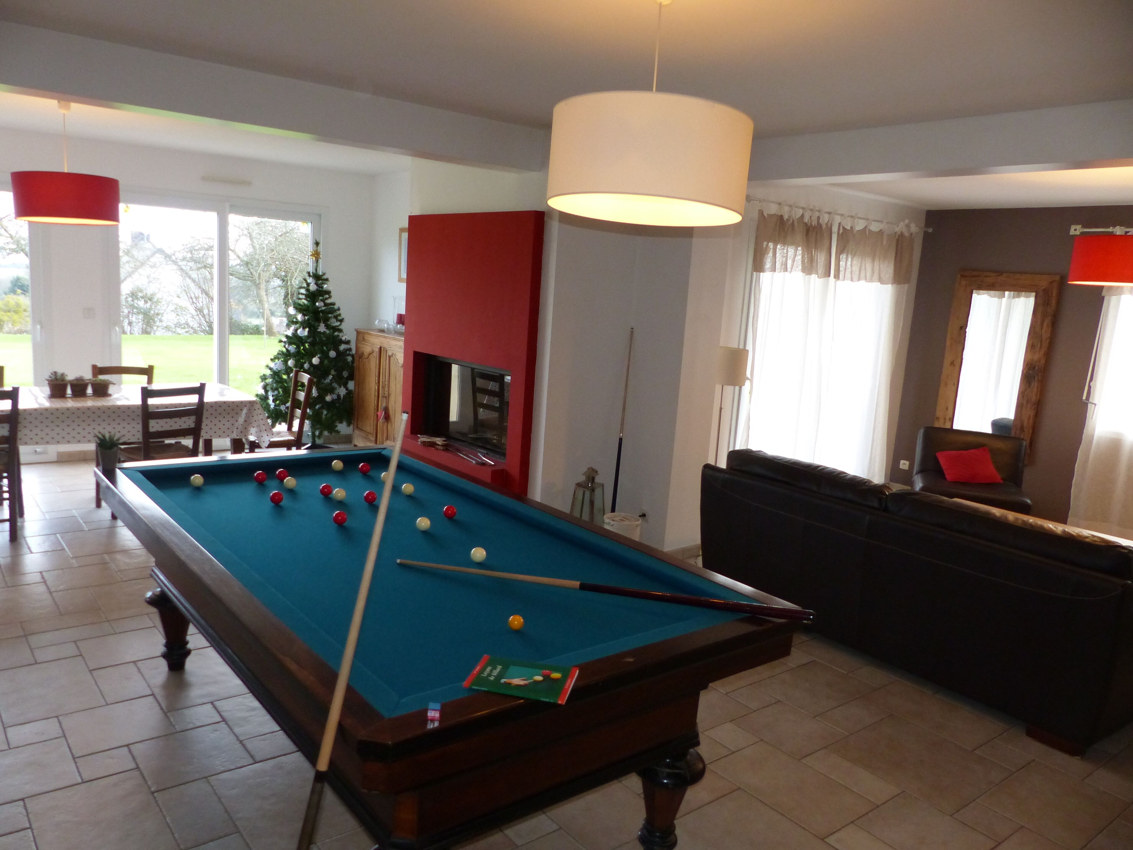 A pool table in a living room with a red wall, a sofa, and a Christmas tree.
