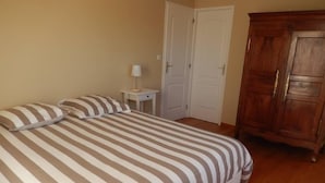 A bedroom with a large bed, two pillows, a nightstand with a lamp, a wooden wardrobe, and a white door. - HOUSE WITH SEA VIEW ON NICE PLOT (Crasville)