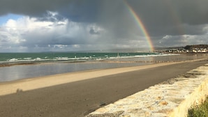 A beach with a rainbow, a stormy sky, and a distant shoreline with buildings. - HOUSE WITH SEA VIEW ON NICE PLOT (Crasville)