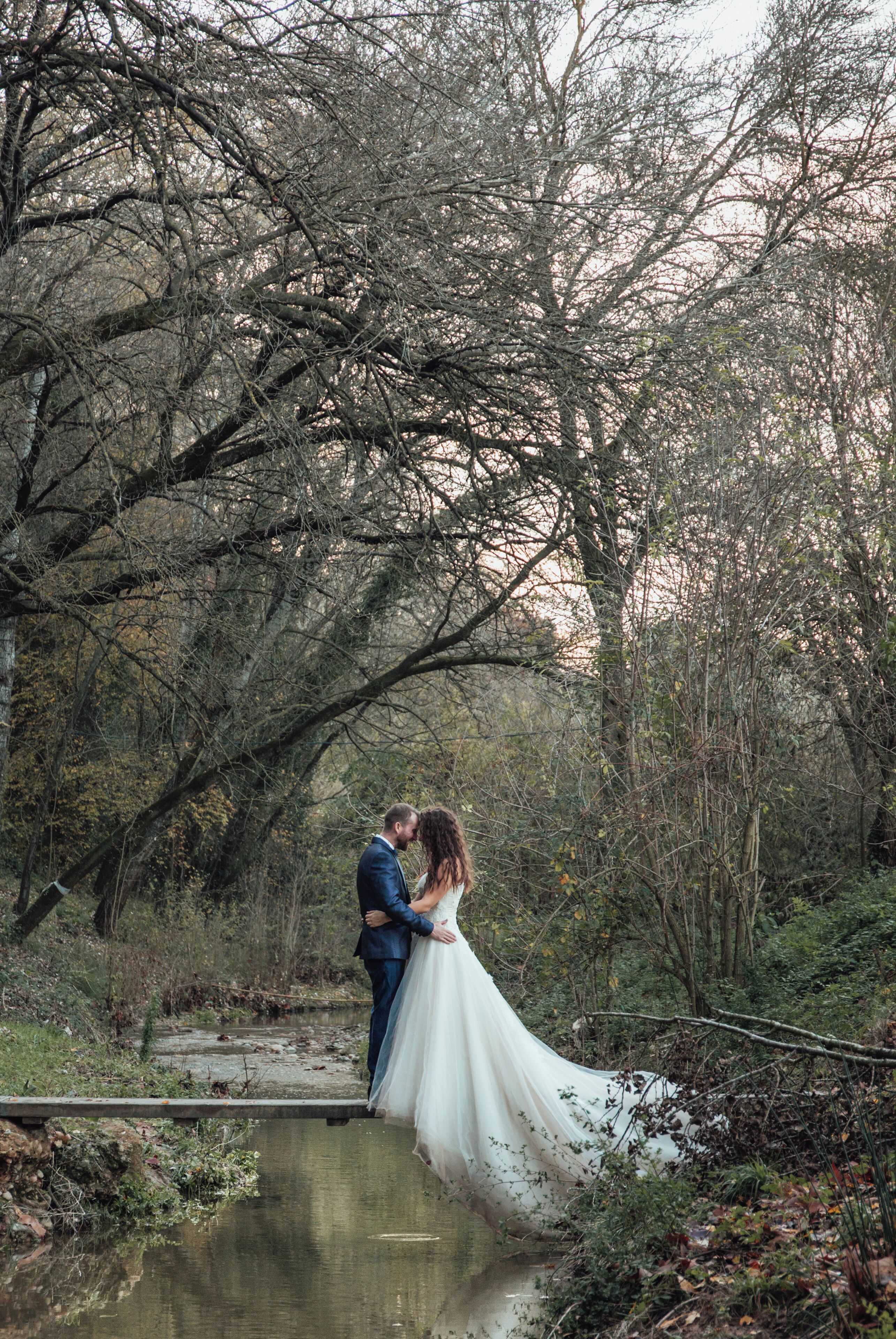 A couple embracing by a calm river in a wooded area.