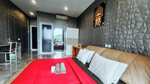 A modern hotel room with a large bed, a red blanket, and a Buddha painting on the wall. - Margarita Surf Hostel Canggu (Pererenan)