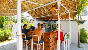An outdoor bar area with wooden seating and a thatched roof. - Margarita Surf Hostel Canggu (Pererenan)
