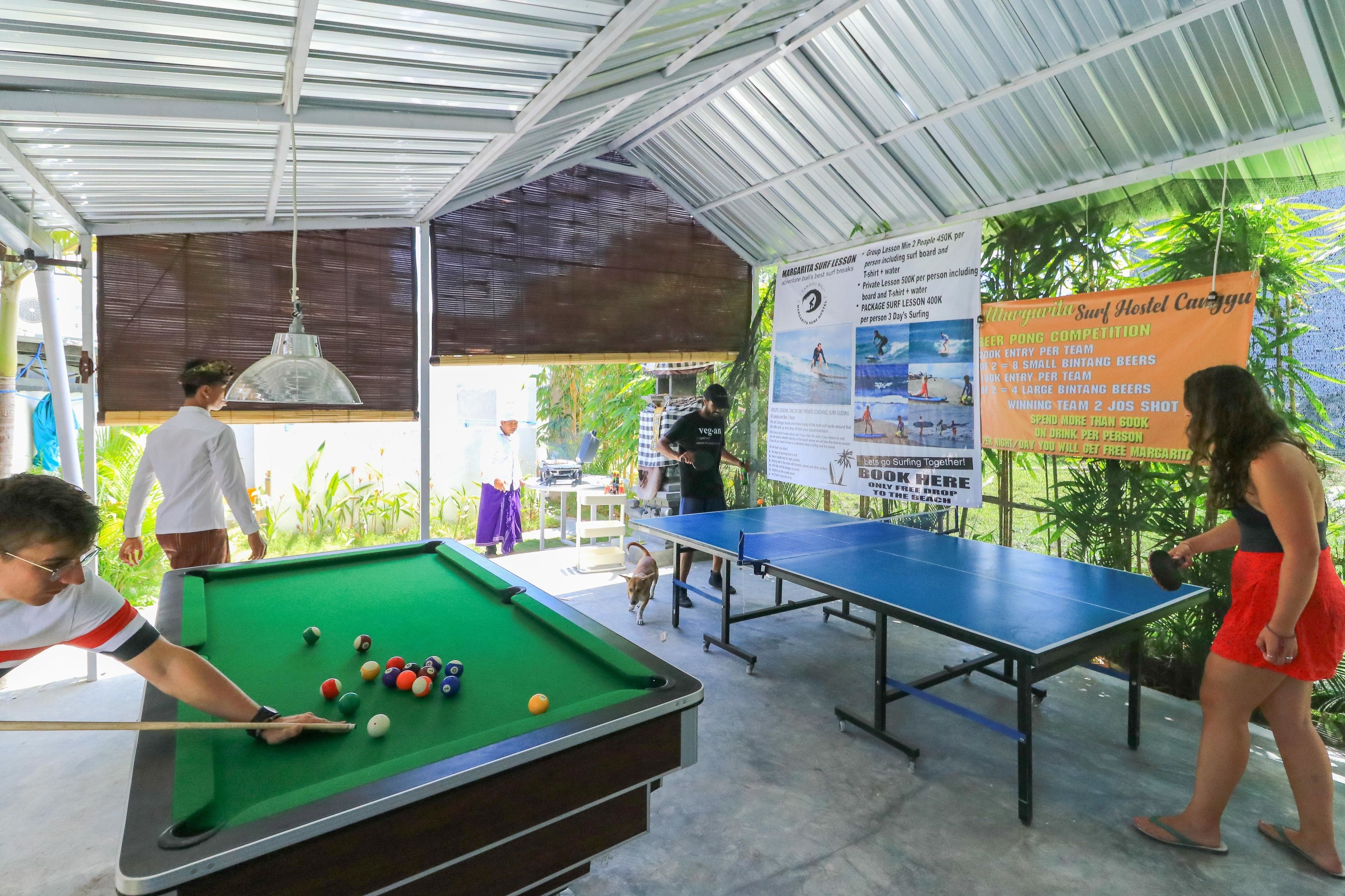 A pool table and a ping pong table in an outdoor area with a covered roof.