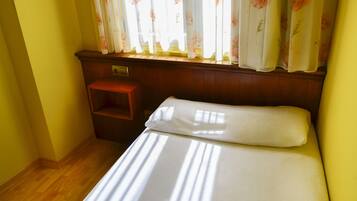 Una habitación con una cama, una mesita de noche de madera y una ventana con cortinas florales.