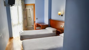 A hotel room with two single beds, a wooden nightstand, a small table, a TV mounted on the wall, and a shower area visible through an open door. - Alda Vía de la Plata Rooms (La Baneza)