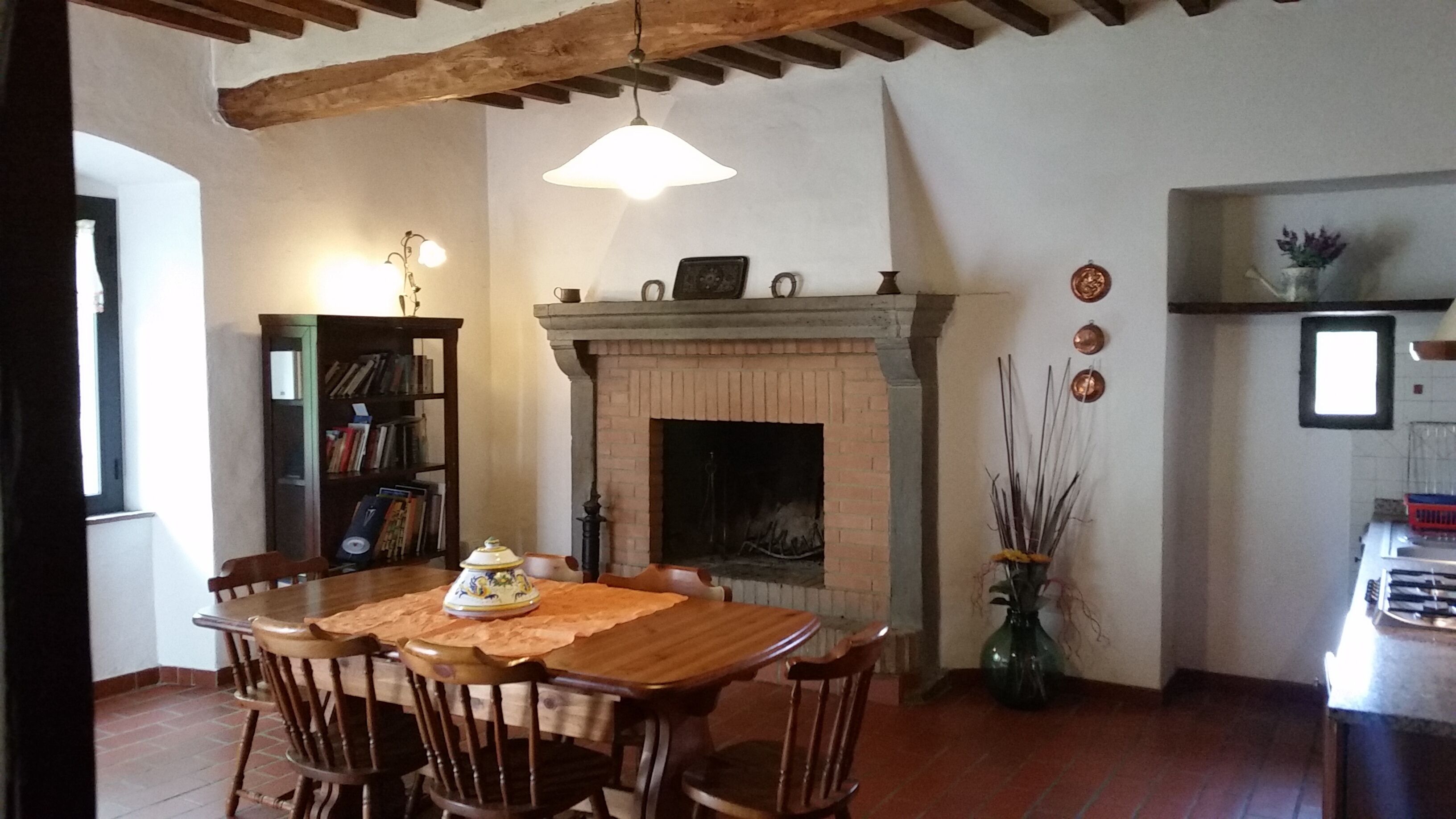A dining area with a wooden table and chairs, a fireplace, a bookshelf, and a hanging light fixture.