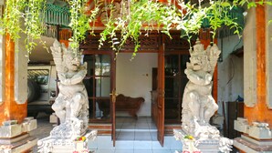 A traditional building entrance with two stone lion statues, a wooden door, and a tiled floor. - Inada Losmen (Seminyak)