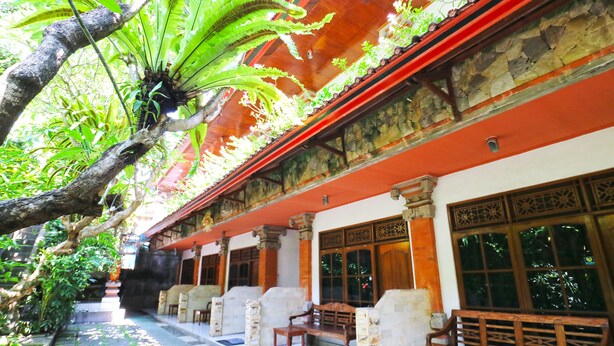 A traditional building with stone pillars, wooden benches, and a covered walkway. - Inada Losmen (Seminyak)