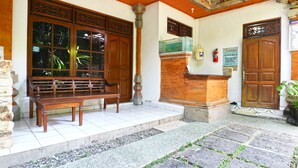 A traditional building with a wooden bench outside, a reception desk, and a fire extinguisher. - Inada Losmen (Seminyak)