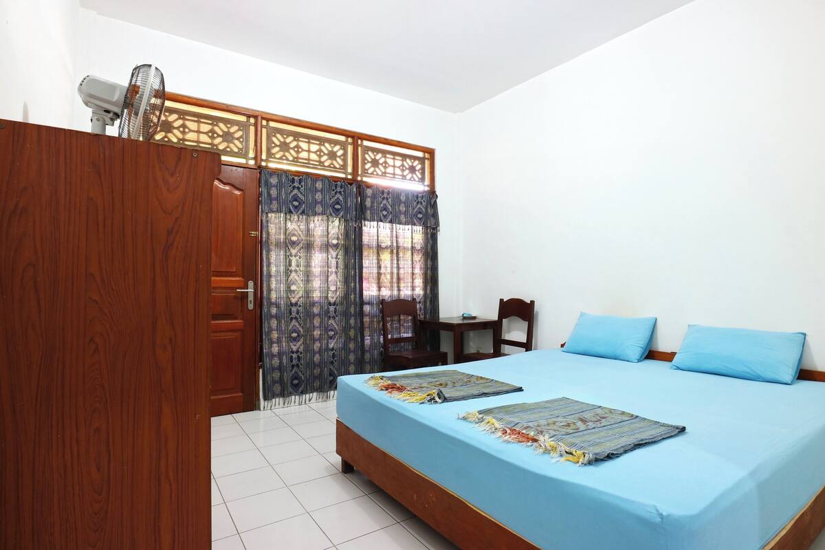 A bedroom with a bed, a wooden wardrobe, a desk, and a chair.