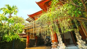 A traditional building with a covered entrance, a parked vehicle, and lush greenery. - Inada Losmen (Seminyak)