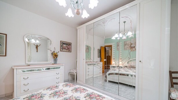A bedroom with a large mirror, a dresser, a bed, and a chandelier.