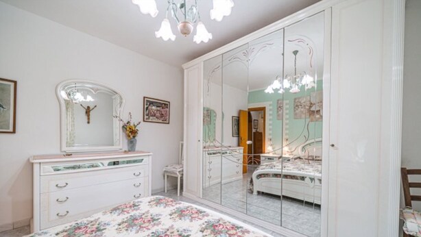 Un dormitorio con un espejo grande, un aparador, una cama y una araña.