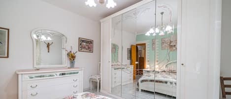 A bedroom with a large mirror, a dresser, a bed, and a chandelier.