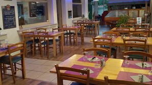 Un restaurante con mesas y sillas de madera, asientos con cojines azules e iluminación colgante.
