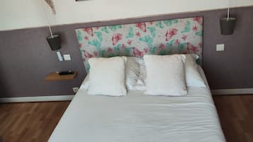Una cama bien hecha con ropa blanca, un cabecero estampado con motivos florales y dos mesitas de noche fijadas a la pared con lámparas.