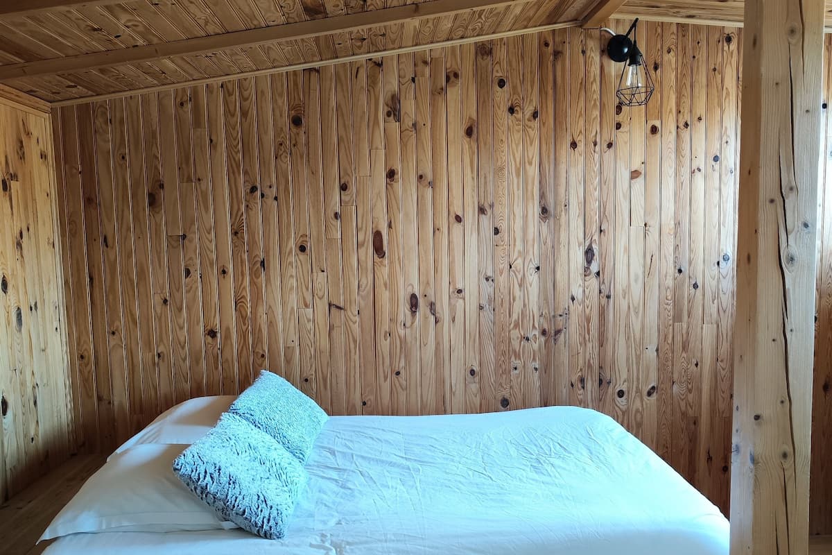 A wooden room with a bed, a ceiling fan, and a wooden floor.