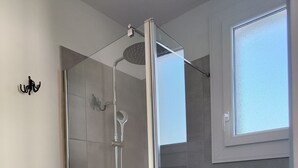 Una ducha moderna con puerta de cristal, cabezal de ducha manual y lavamanos portátil.