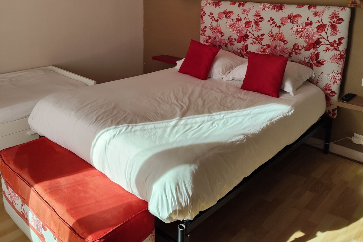 A neatly made bed with white and red bedding, a round mirror on the wall, and a wooden floor.