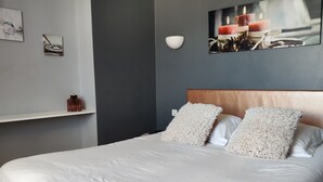 Un dormitorio moderno con una cama grande, cabecera, luz empotrada en la pared y un cuadro enmarcado.