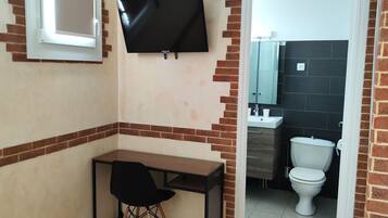 Una habitación pequeña con escritorio, silla, televisión y vista al baño.