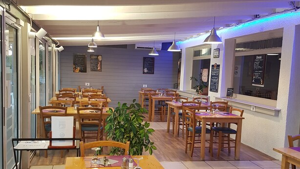 Un restaurante con mesas y sillas de madera, una planta en maceta y pizarras con la carta.