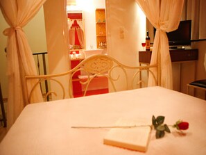 A bed with a white headboard, a bedside table, and a single red rose on the bed. - Ann George Resort (Lesvos)
