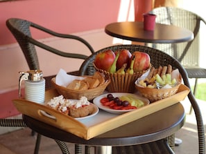 A tray with various food items including bread, cheese, fruits, and olives on a wicker chair outdoors. - Ann George Resort (Lesvos)