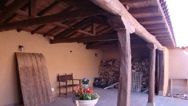 A covered outdoor area with a wooden bench, a large planter with flowers, and a stack of firewood. - Hotel Rural Betania (Villamol)