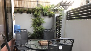 A glass-top table with four black chairs, surrounded by potted plants and a bamboo fence. - Lighthouse Apartment and Guest Inn (Puerto Princesa)