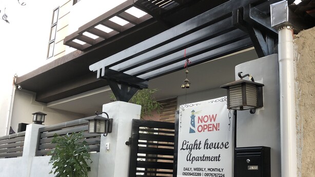 A light house apartment with a black gate, a welcome sign, and a potted plant. - Lighthouse Apartment and Guest Inn (Puerto Princesa)