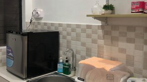 A kitchen with a black refrigerator, a sink, a Megabox dish rack, and a shelf with toiletries. - Lighthouse Apartment and Guest Inn (Puerto Princesa)