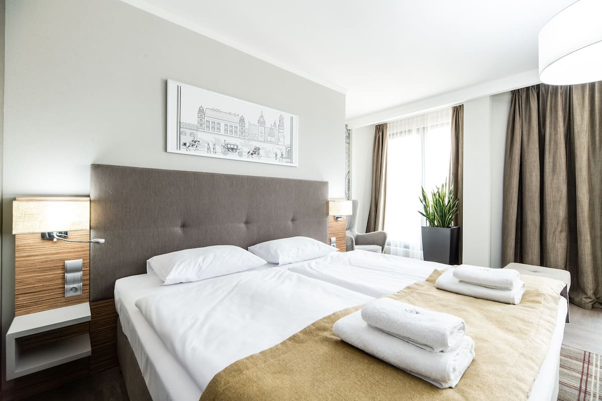 A hotel room with a large bed, a bedside table with a lamp, a wall-mounted artwork, and a window with curtains.