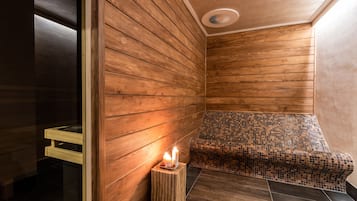 Een houten sauna met een bank, een klein tafeltje met kaarsen en een betegelde vloer.
