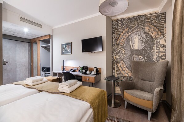 A hotel room with two beds, a desk, a chair, a TV, and a patterned wall. - Perfect Hotel (Kraków)