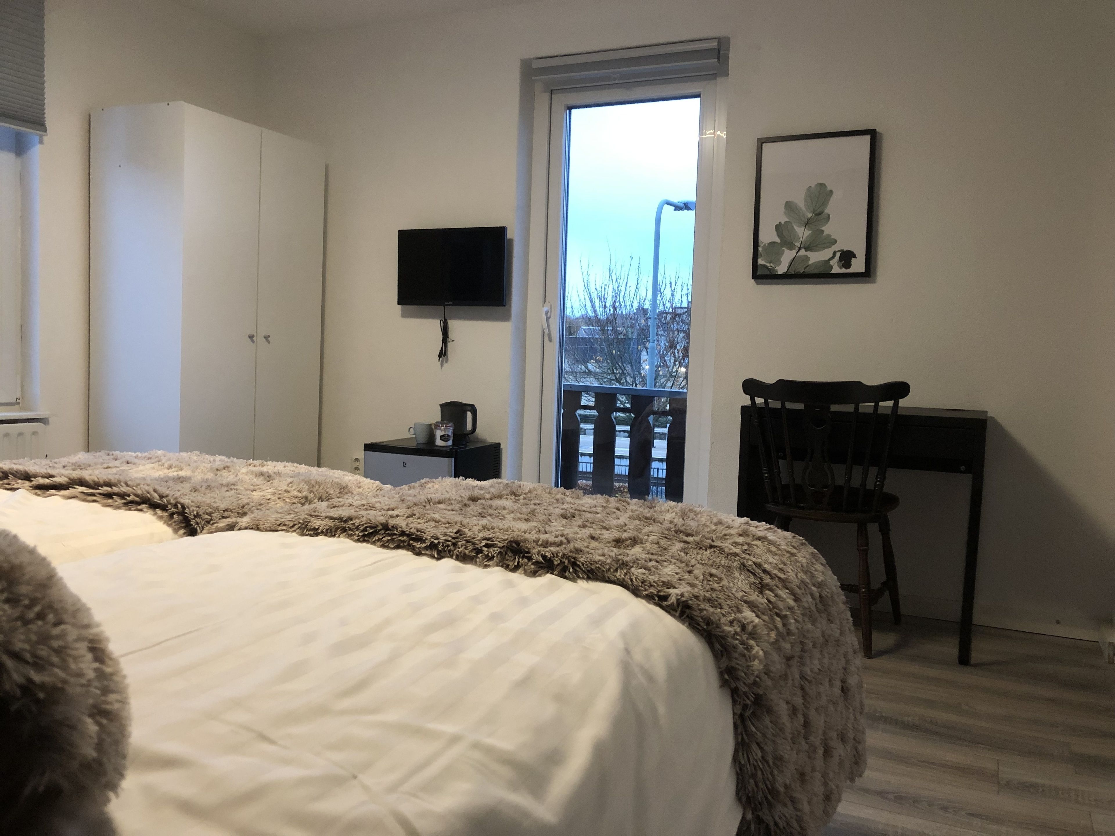 A bedroom with a bed, a desk, a chair, a TV, and a window with a view of the outside.