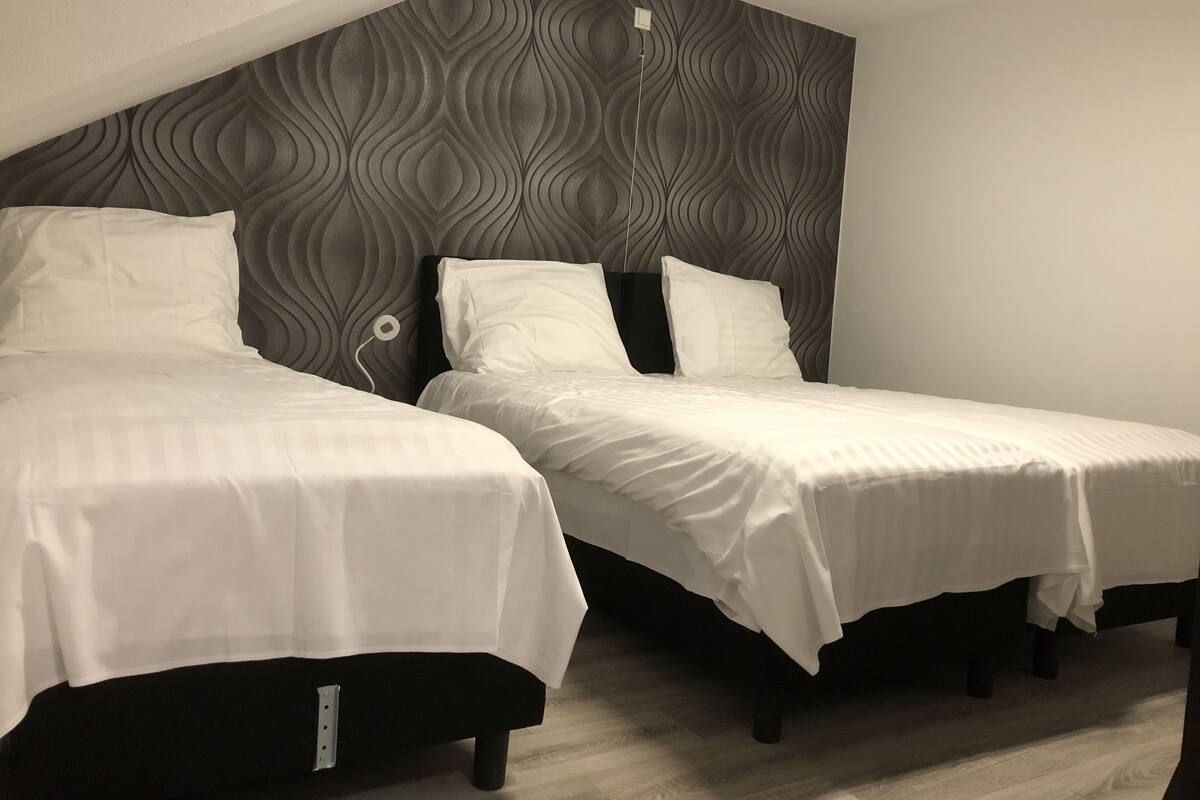 Two single beds with white bedding, a grey patterned headboard, and a wooden floor.