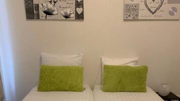 Een kamer met twee eenpersoonsbedden, elk met een groene kussen en een witte kussen. Twee kunstwerken hangen aan de muur, waarvan één de tekst 'LOVE' bevat en de ander harten en de tekst 'Love'.