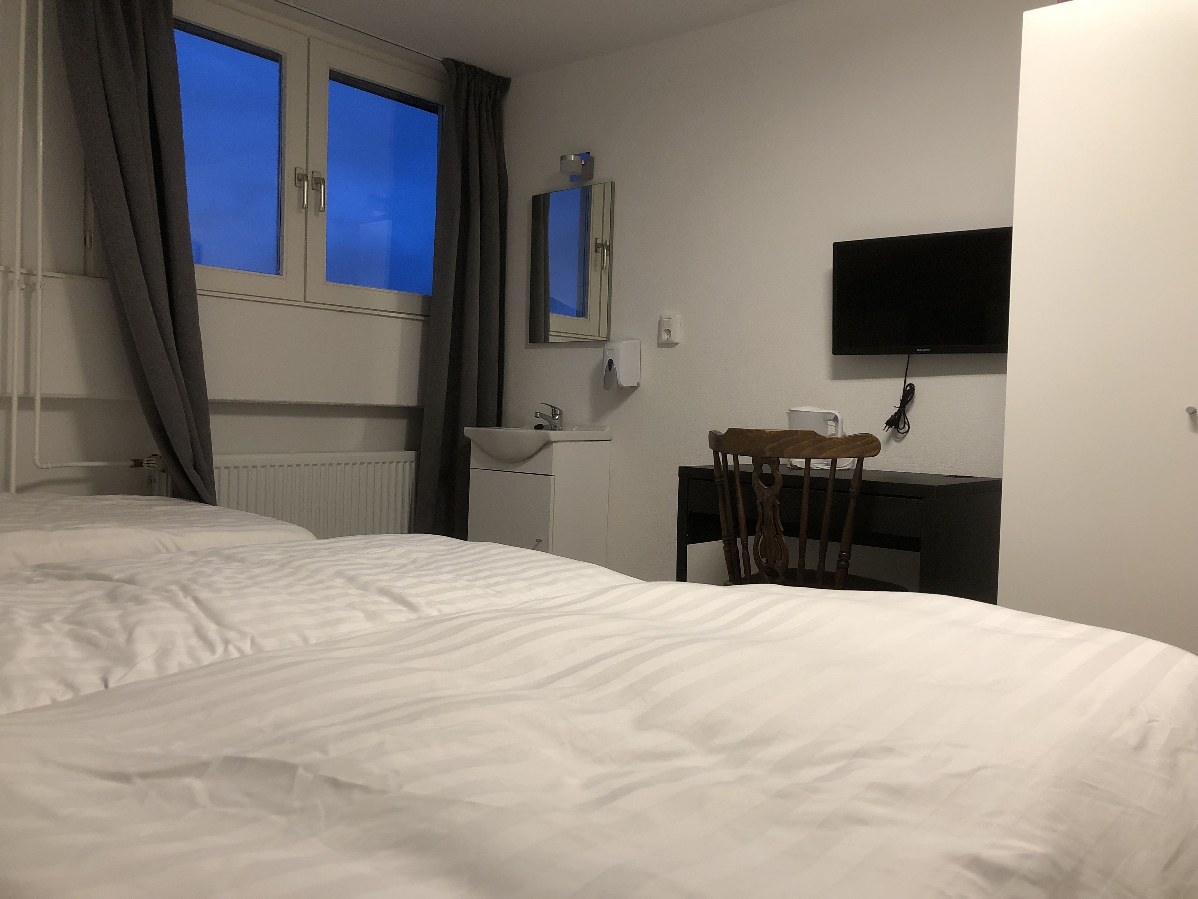 Une chambre d’hôtel comprenant un lit, un bureau avec une chaise, un téléviseur à écran plat fixé au mur et une fenêtre avec des rideaux.
