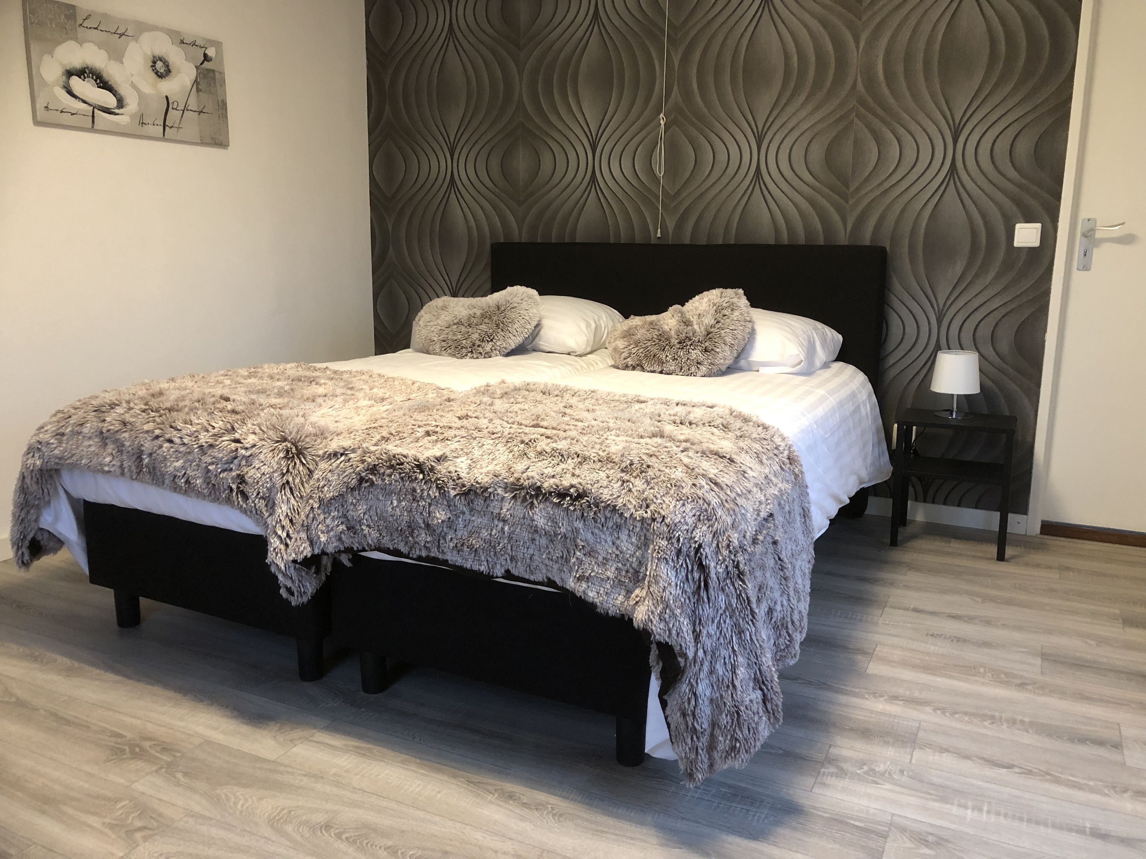 Un dormitorio con una cama, una mesita de noche, una lámpara y una pared con textura.